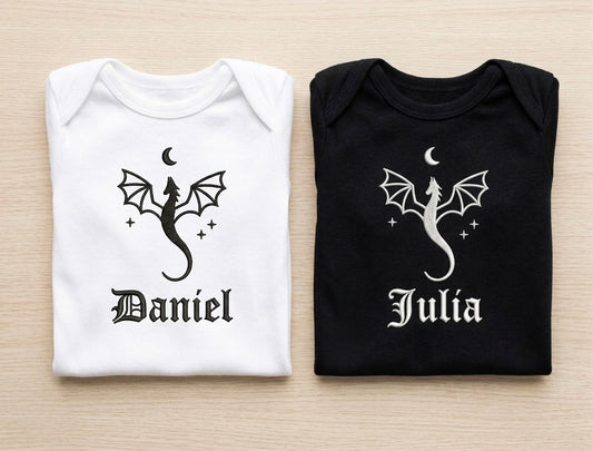 Two folded shirts, one white and one black, with dragon designs and names 'Daniel' and 'Julia' on a light wooden surface.