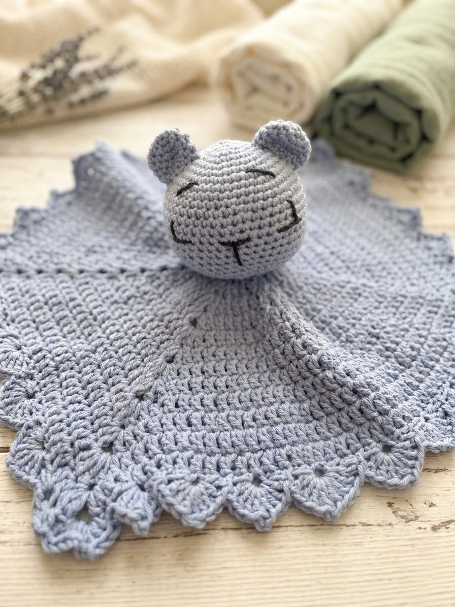 Crocheted blue blanket with a bear-shaped security blanket on top, set against a neutral background.