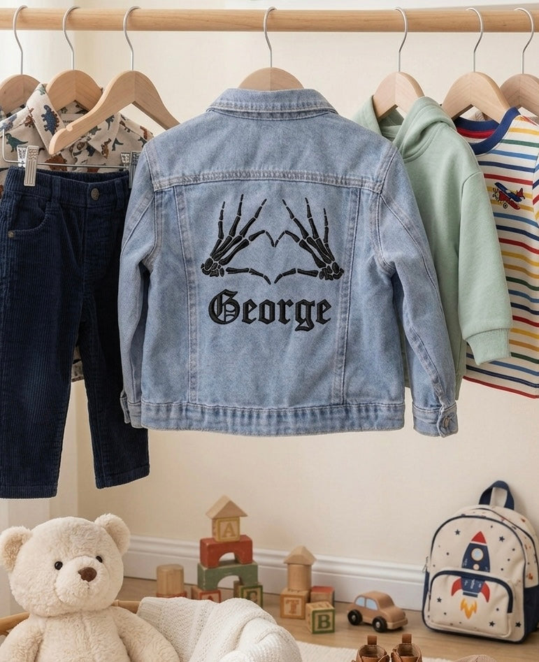 Children's denim jacket with 'George' design, hanging on a rack with other children's clothing.