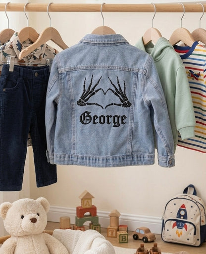 Children's denim jacket with 'George' design, hanging on a rack with other children's clothing.