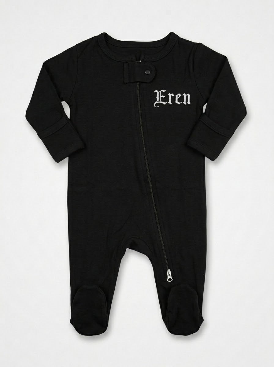 A black baby footed sleeper with long sleeves, a front zipper, and the name 'Eren' embroidered in a white gothic font on the left chest, displayed flat against a light gray background.