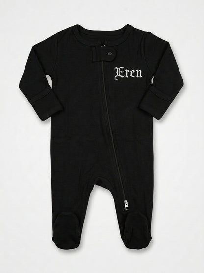 A black baby footed sleeper with long sleeves, a front zipper, and the name 'Eren' embroidered in a white gothic font on the left chest, displayed flat against a light gray background.