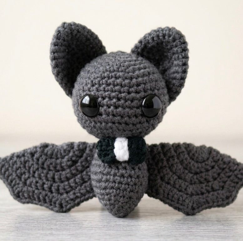 Shadow grey amigurumi crochet bat plush next to gothic safety pins and checkers.