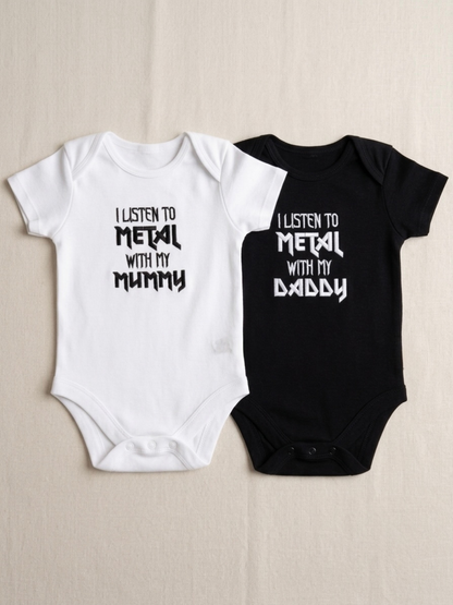 Two baby short-sleeve bodysuits laid flat on a light beige background: one white with black embroidered text reading 'I LISTEN TO METAL WITH MY MUMMY' and one black with white text reading 'I LISTEN TO METAL WITH MY DADDY'.