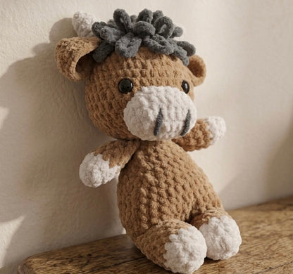 Handmade Crocheted highland cow stuffed toy with a textured head on a wooden surface